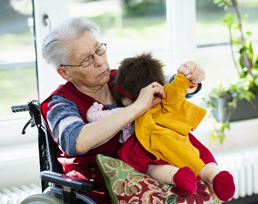 Une personne âgée changeant les vêtements d'une poupée d'empathie Une personne âgée changeant les vêtements d'une poupée d'empathie